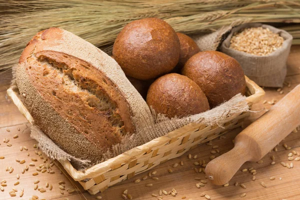 Assortment of fresh bread in a basket on a wooden table, composition with additional accessories — Stock Photo, Image