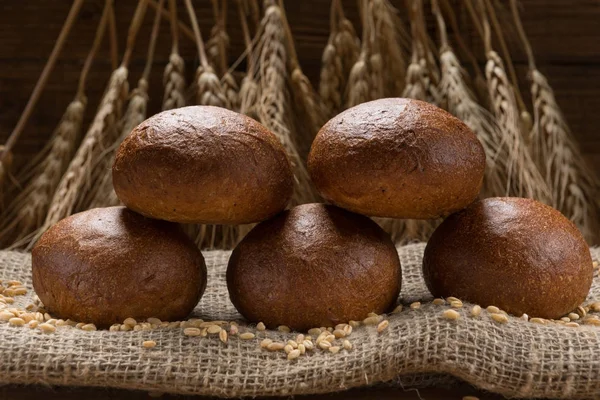 Five buns lined up in a sackcloth, in the background wheat ears — Stock Photo, Image