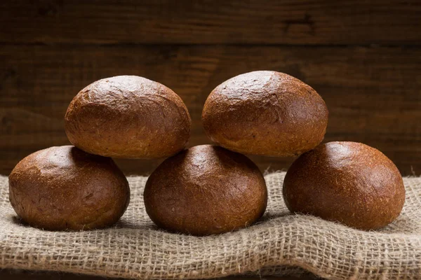 Five buns lined up in a sackcloth, in the background wooden boards — Stock Photo, Image