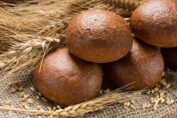 Five buns lined up in a sackcloth, in the background wheat ears — Stock Photo, Image