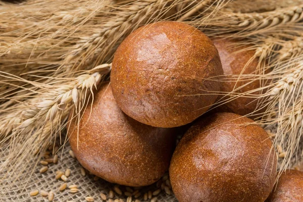 Five buns lined up in a sackcloth, in the background wheat ears — Stock Photo, Image