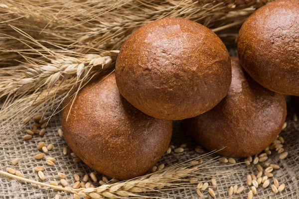 Five buns lined up in a sackcloth, in the background wheat ears — Stock Photo, Image