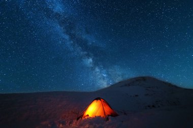 Çadırları olan turistlerin arka planında parlak Samanyolu ile uzay yıldızlı geceler.