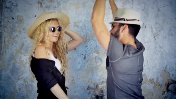 Feliz pareja joven en gafas de sol y sombreros bailando en cámara lenta escuchando música divirtiéndose en el amor . — Vídeo de stock
