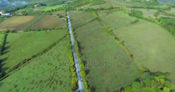 Vista panoramica dall'alto su strada forestale, campi e bosco, un edificio sullo sfondo. La macchina si sta muovendo lungo la strada. Colpo aereo . — Video Stock