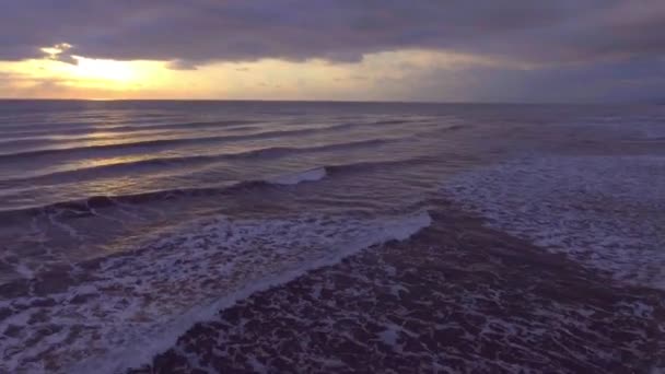 Vlucht over de zee met schuim golven bij zonsondergang op de achtergrond een kustlijn en een dok, schieten vanuit een helikopter — Stockvideo