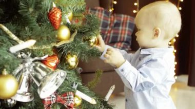 Etkin şirin çocuk bir koltuk ve çelenk oyuncak topları arka planda rahat bir ev iç bir Noel ağacı üzerinde çalış