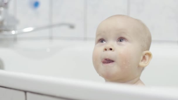 Маленька мила дитина приймає ванну крупним планом, дивиться вгору і показує мову, дитина виглядає цікаво вгору — стокове відео