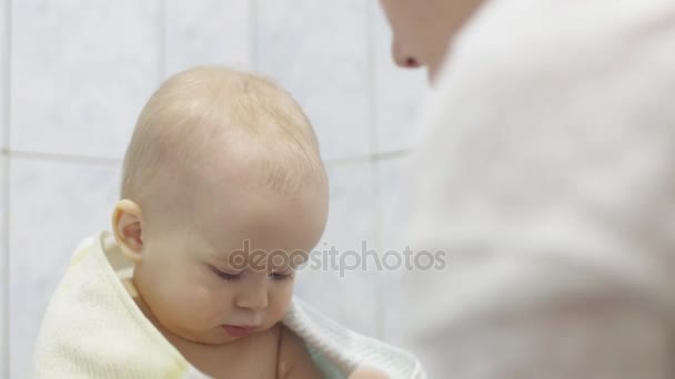 Kleine baby na het nemen van een bad zit een stuk speelgoed bedrijf, een liefdevolle moeder veegt het kind met een handdoek — Stockvideo