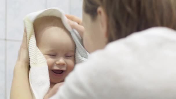 Omtänksam mor torkar sitt barn med en handduk efter tvätt, en söt baby innehar en leksak i handen — Stockvideo