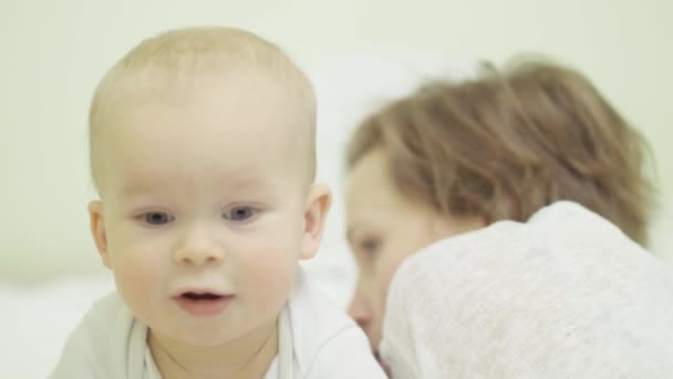 Retrato de un niño feliz sonriendo y riendo, mirando hacia adelante, en el fondo, madre acostada sobre una manta suave — Vídeos de Stock