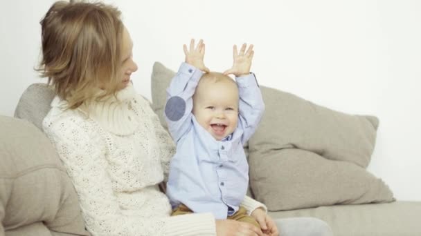 Веселая счастливая мать и маленький сын наслаждаются смехом и хорошим настроением, сидя дома на диване — стоковое видео