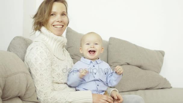 Portrait de mère heureuse et bébé assis sur le canapé, souriant et riant, regardant droit devant — Video