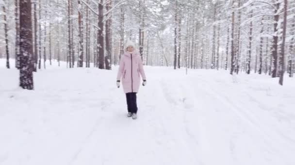 Menina agradável em roupas quentes de inverno caminha pela floresta no inverno durante o dia — Vídeo de Stock