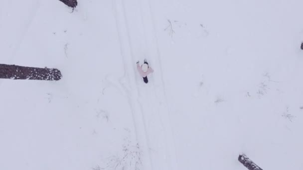 Aerial shot active girl walking along the path in the winter snow forest, shooting from the helicopter — Stock Video