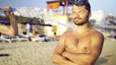 Siyah saçlı genç Avrupa adam sahilde su dökün ve kum mizahi bir şekilde at. Ağır çekim