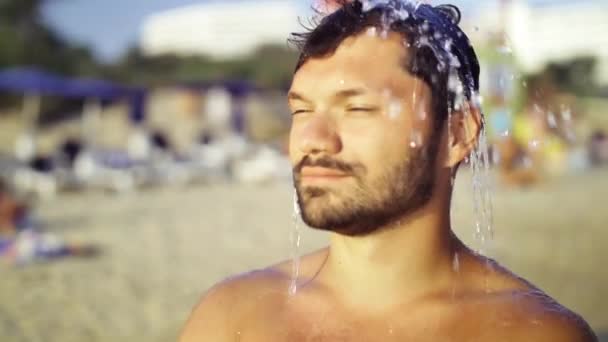 Retrato de un hombre europeo bronceado en verano en la playa. Pulverización de agua en un ambiente de enfriamiento en la playa. En cámara lenta. Salpicaduras de agua refrescante . — Vídeo de stock