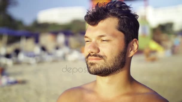 Retrato de un hombre europeo despreocupado mirando a la distancia para disfrutar del sol y el mar en la playa. Movimiento lento — Vídeos de Stock