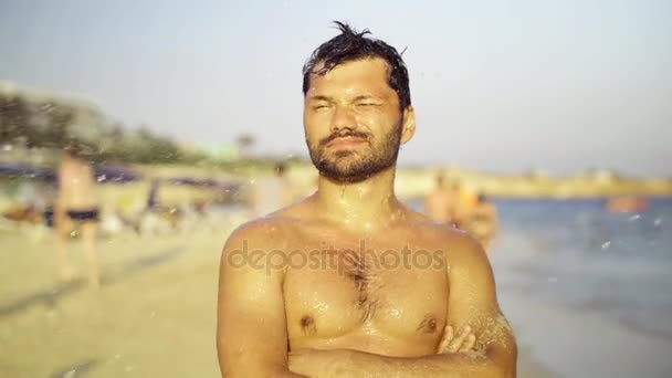 Молодой человек на пляже, брызгает водой в юмористической комической форме. Медленное движение — стоковое видео