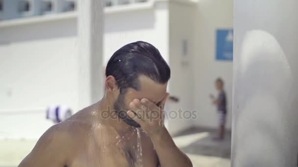 El hombre europeo toma una ducha en un lugar público en la playa, salpicaduras de agua vuelan en diferentes direcciones. Movimiento lento — Vídeos de Stock