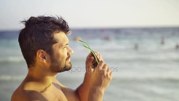 Der europäische Sportler genießt den Blick auf Sonne und Meer, setzt sich eine Sonnenbrille auf, im Hintergrund das Meer und die Wellen. Zeitlupe — Stockvideo
