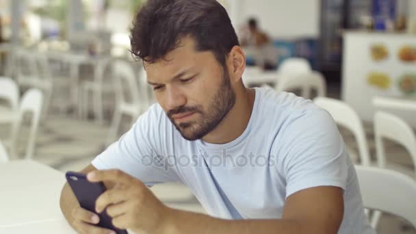 L'uomo bruna europeo seduto a tavola nel caffè usa smartphone, guarda lo schermo del telefono, scrive messaggi, primo piano — Video Stock