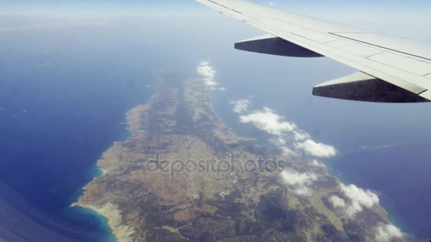 Colpo aereo. Viaggiare in aereo. Guarda attraverso il finestrino dell'aereo. Volo sul mare azzurro e un'isola in mezzo al mare — Video Stock