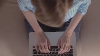 Yukarıdan aşağı, yüksek açı kafasını oturan bir dizüstü eğik metin kullanım yazarak bir dizüstü bilgisayar onun kucağına tutan meşgul genç bir kadın