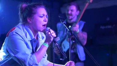 Genç güzel kadın bir mikrofon tutan bir şarkı söylerken sahnede arka plan bas gitarist, yavaş hareket durumda