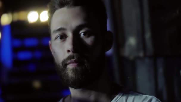 Retrato de un joven serio con barba y un peinado de moda en un club nocturno durante una actuación musical de una banda de rock. Disparo bajo llave . — Vídeos de Stock