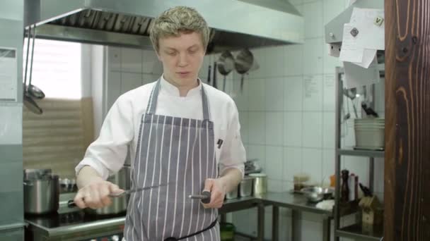 Chef de tiro medio agudiza un cuchillo profesional de acero afilado en la cocina de la cafetería del restaurante, cámara lenta — Vídeo de stock