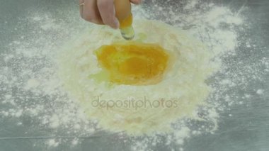 Erkek el un içine çiğ yumurta kırmak. Hamur hazırlık süreci yavaş hareket, yakın çekim. Yumurta un bir yığının üstüne düşüyor