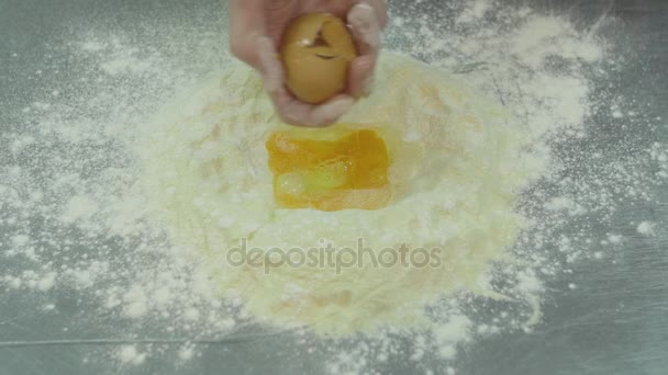 Les mains masculines cassent les œufs en farine. Chef pétrit la pâte dans la farine sur la table fermer. Oeuf tombe sur un tas de farine — Video