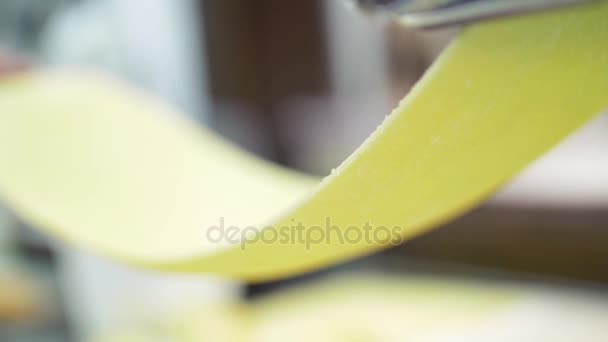 Typische Teigzubereitung für Pasta. Küchenhände halten den Teig in Zeitlupe aus der Nudelmaschine, Nahaufnahme. — Stockvideo