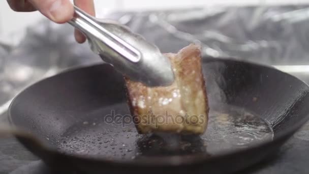 Σεφ χρησιμοποιεί λαβίδες για να μετατρέψει την μπριζόλα τηγανητό ζουμερό κρέας σε ένα τηγάνι, αργή κίνηση, εσωτερικη — Αρχείο Βίντεο