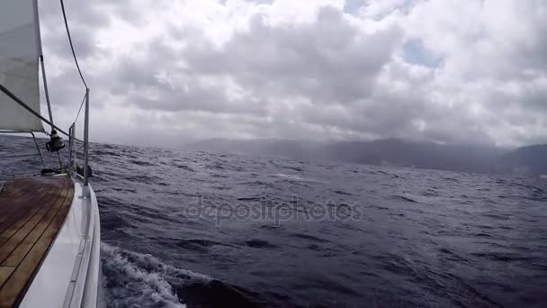 Sailing yacht approach the shore with a mountainous terrain in cloudy weather. Traveling on a yacht. POV — Stock Video
