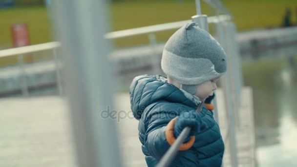 Liten söt baby har en promenad, stående på vattnet, tittar på dammen i svalt väder Slow Motion — Stockvideo