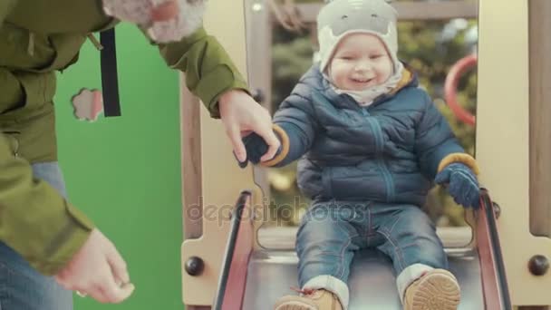Vorsichtige Mutter und glückliches Kind auf dem Spielplatz. Kleiner Junge rollt vom Hügel herunter. Zeitlupe — Stockvideo