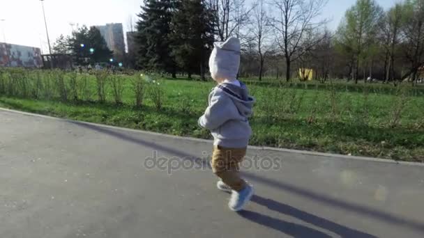 Маленький милый мальчик с уверенными быстрыми шагами прогулки по аллее в парке летом при солнечном свете — стоковое видео