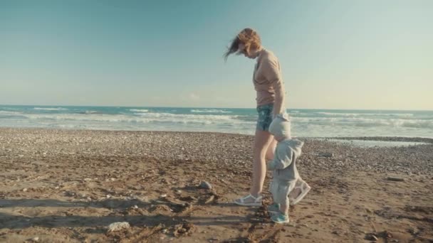 SLOW MOTION Caring mother and little son holding hands walk along the empty shore near the sea — Stock Video