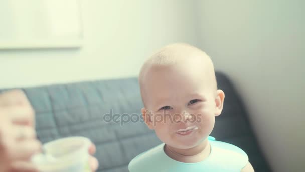 Медленная мама кормит веселого улыбающегося ребенка ложкой. Маленький счастливый мальчик за завтраком — стоковое видео