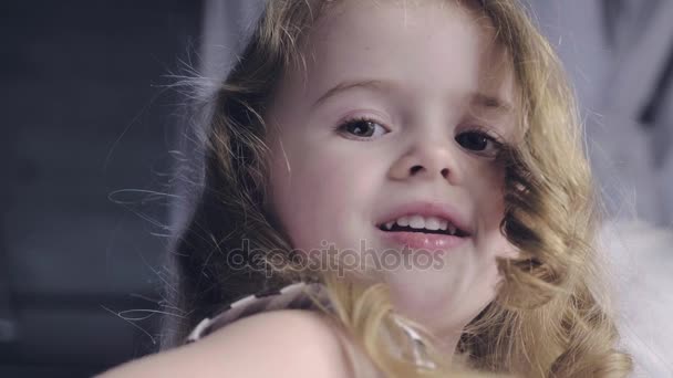 MOCIÓN LENTA: Retrato de cerca de una linda niña sonriente con el pelo rizado largo, ángulo bajo — Vídeo de stock