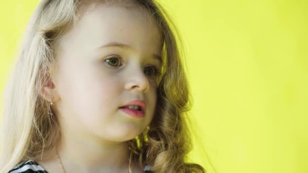 Linda niña sonriente con el pelo rizado. Retrato de primer plano sobre fondo amarillo. Movimiento lento — Vídeos de Stock