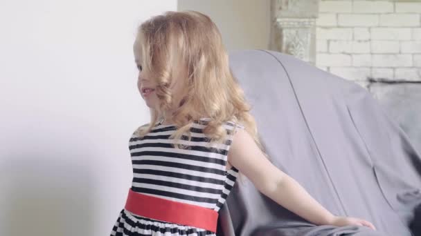 Кокетливая маленькая симпатичная девочка, позирующая для фотосессии в помещении, на заднем плане стул, замедленная съемка. — стоковое видео
