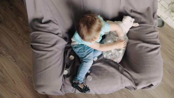 Child sitting in a large armchair plays with decorative candles, taking them out of the jar, slow mo — Stock Video