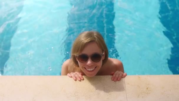 Lächelnd braun gebrannte schöne Reisemädchen mit Sonnenbrille, die im Swimmingpool schwimmt — Stockvideo