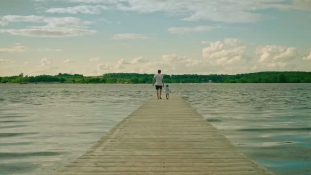 Baba ve küçük kız nehirdeki tahta iskelede el ele yürüyorlar. — Stok video