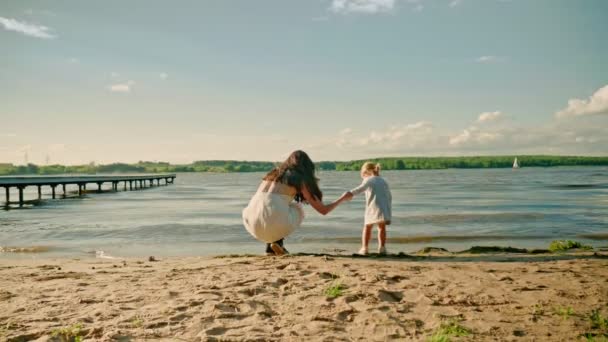 Mutter spielt mit reizender Tochter am Sandstrand in der Nähe der Seebrücke — Stockvideo