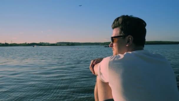 Hombre con gafas de sol relojes hermoso río al atardecer — Vídeo de stock