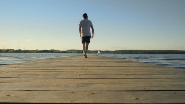 Young man walks on long wooden river pier slow motion — Stock Video